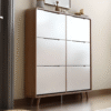Modern wooden shoe cabinet by WoodBee Craft featuring six high-gloss white tipping bucket doors, rounded corners, and tapered legs in a bright hallway entryway.