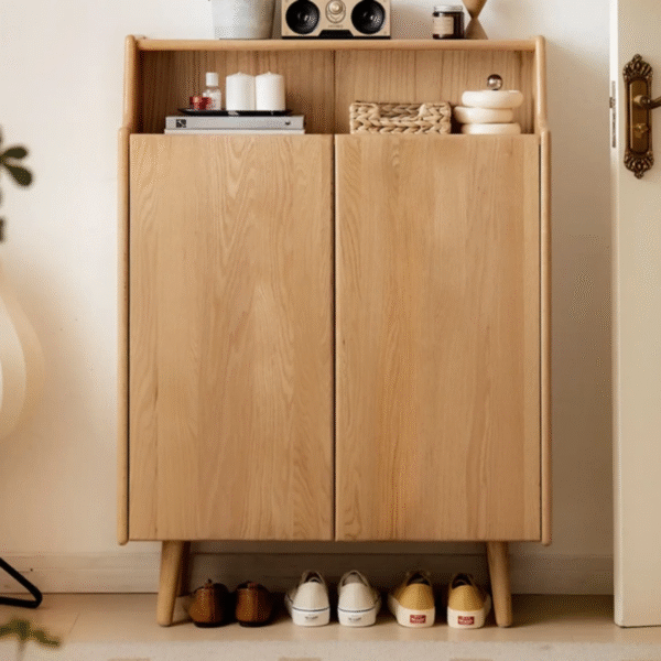Freestanding wooden shoe cabinet by WoodBee Craft in a natural oak finish, featuring handleless double doors, an open top shelf with decor, and sneakers parked underneath.